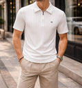Man wearing a white polo shirt and beige shorts standing on a city street.