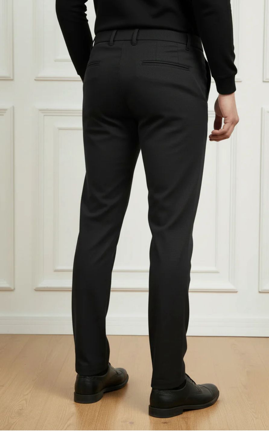 Person wearing black pants standing against a white paneled wall.