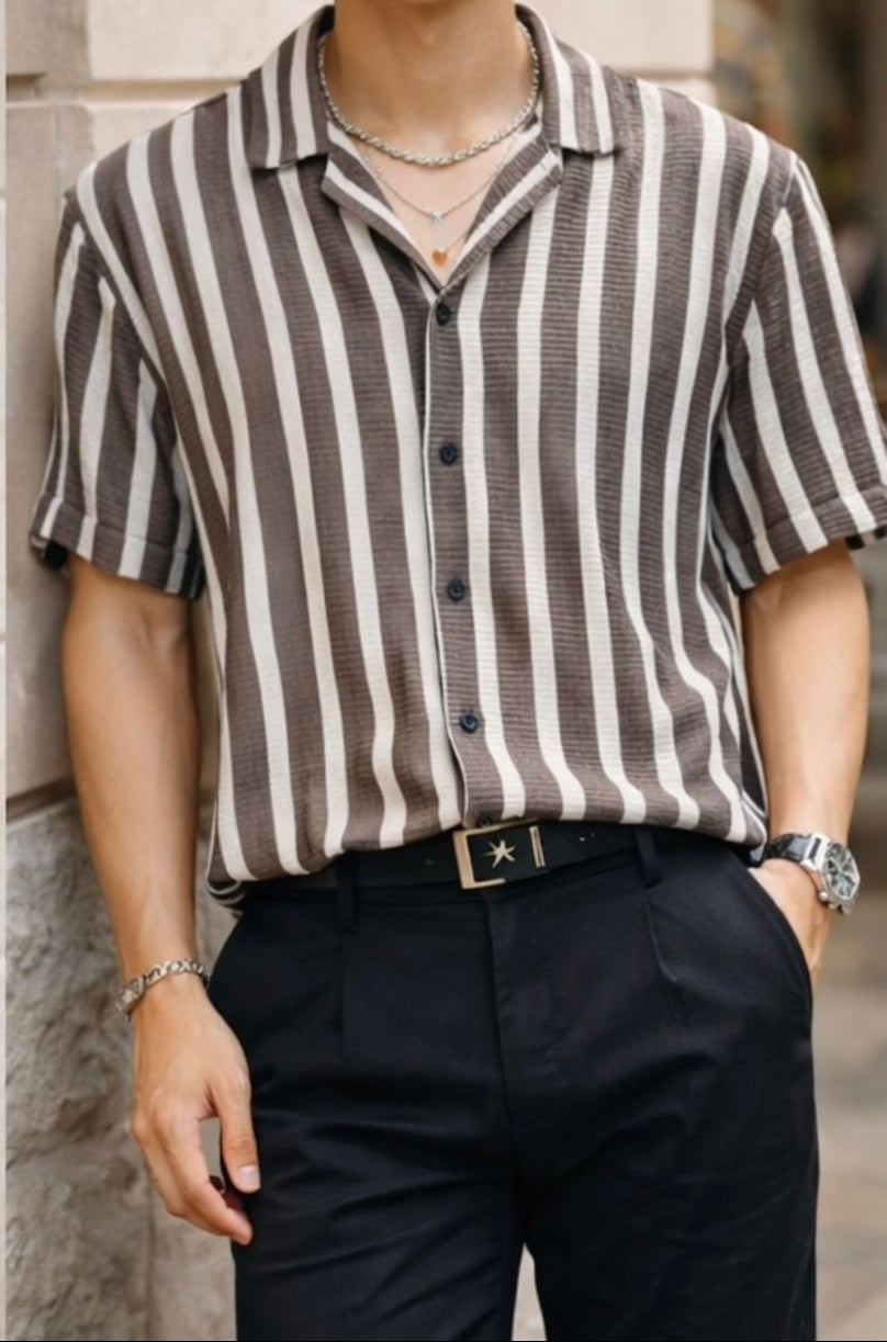 Person wearing a brown and white striped shirt with black pants, standing against a stone wall.