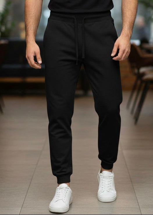 Man wearing a black t-shirt and pants with white sneakers in an indoor setting.