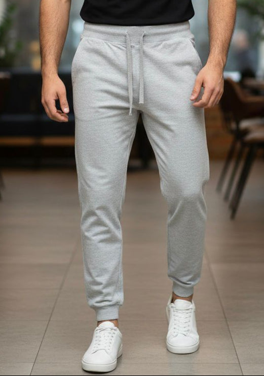 Man wearing a black t-shirt and light gray jogger pants in an indoor setting.