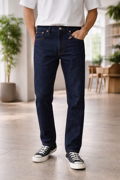 Person wearing dark blue jeans and black sneakers in a room with plants and furniture.