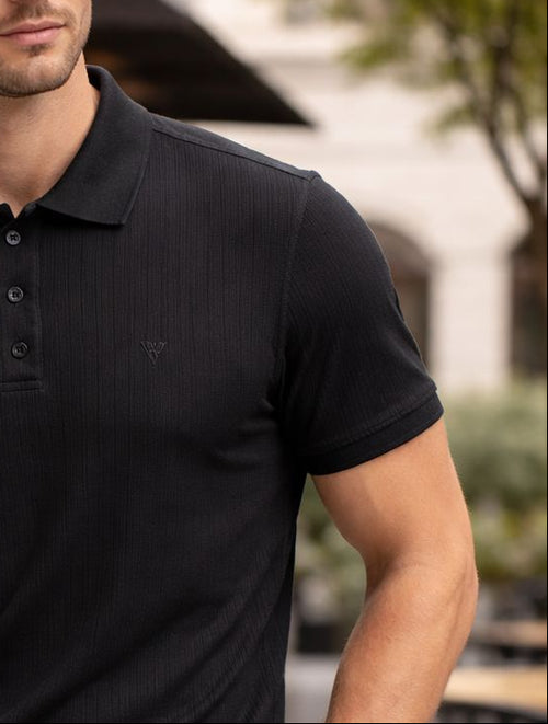 Man wearing a black polo shirt and gray pants outdoors.