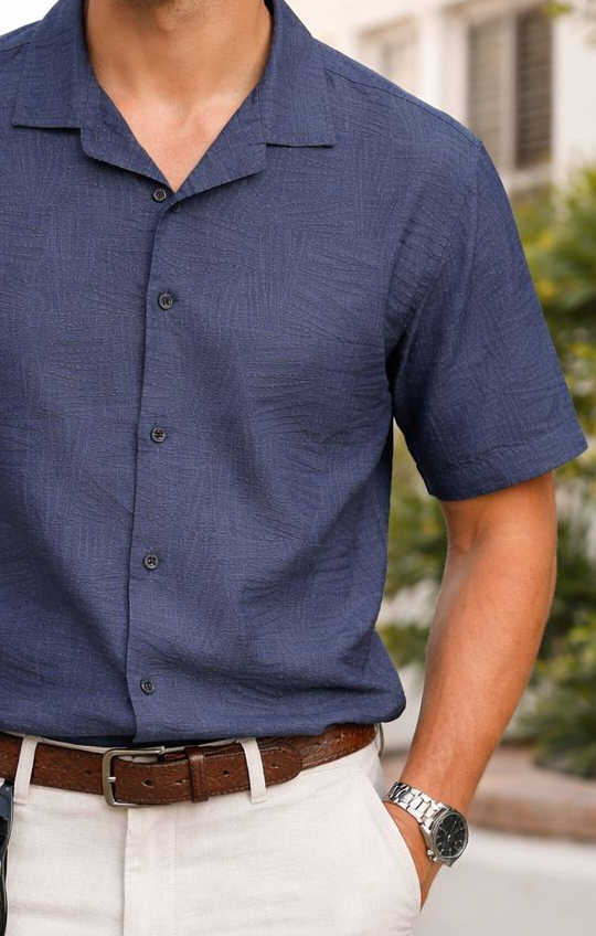 Man wearing a blue shirt and white pants standing outdoors with palm trees in the background