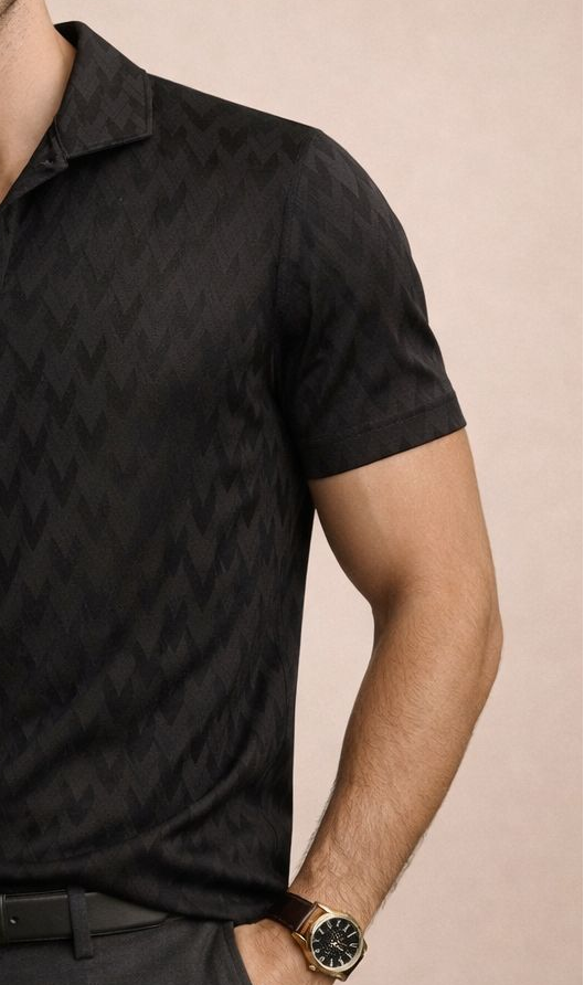 Man wearing a black patterned polo shirt and dark pants against a beige background